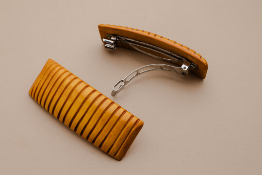 Two elegant wooden hair clips with striped texture and polished metal clasp on a smooth, light beige surface, stylish accessory for hair