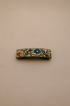 Elegant gold textile hair barrette with vibrant floral embroidery on a neutral background, a charming accessory for various hair styles and fashion