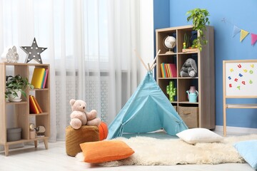 Blue wigwam, colorful pillows, pouf and shelving units in stylish child's room. Interior design © New Africa
