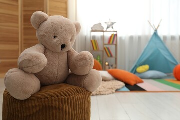 Cute toy bear on pouf in stylish child's room, closeup. Space for text © New Africa
