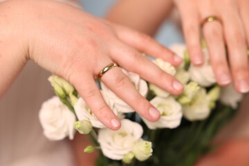 Fototapeta premium Lesbian marriage. Two brides with beautiful flowers showing their wedding rings, closeup