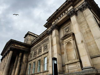 Obraz premium Neoclassical library building in Liverpool with grand stone columns and ornate façade under a cloudy sky with a seagull flying overhead