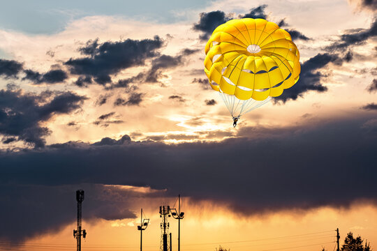 Bright yellow parachute canopy, floating high in the sky against the backdrop of a dramatic sunset with clouds.