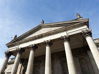 Obraz premium Neoclassical Bank of Ireland building facade with Corinthian columns and rooftop statues in Dublin, Ireland, classical architecture under a clear blue sky