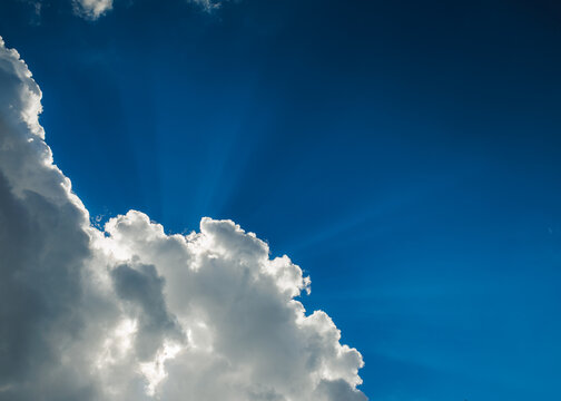 Dramatic blue sky with sun rays shining through fluffy white clouds