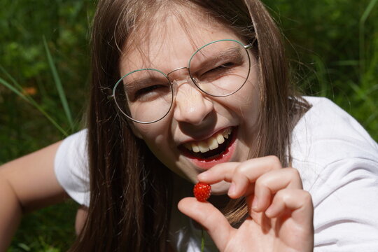 Girl with glasses laughing while eating wild strawberry