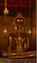Obraz premium Bangkok, Thailand. Inside the temple's main hall is a large golden Buddha statue. There are lamps, an altar, flower arrangements, and warm white light that creates a peaceful atmosphere. Monks are bus