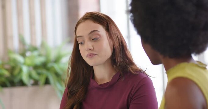 Diverse coworkers in lounge, maroon woman gesturing, showing laptop to explain project details