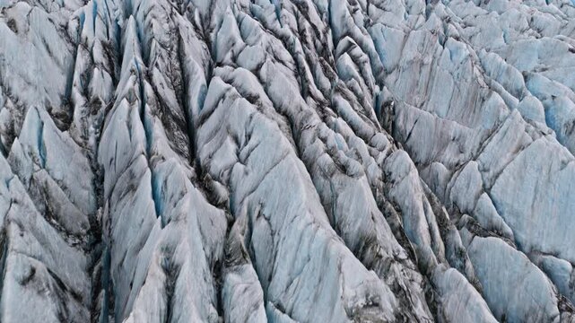 Cinematic drone flyover above abstract blue glacier crevasses and rugged ice formations, revealing striking natural textures, dramatic patterns and frozen landscapes from above.