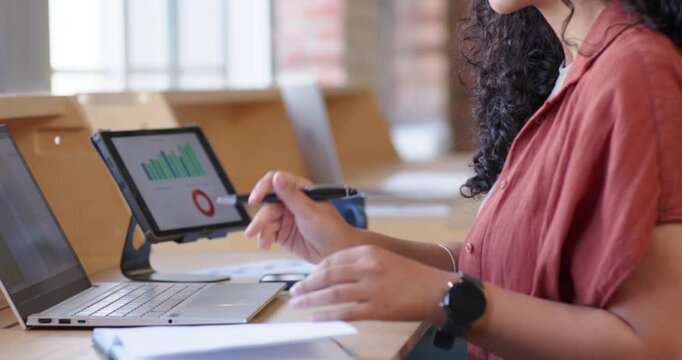 African American woman at desk seeing tablet chart typing laptop using stylus analyzing, copy space
