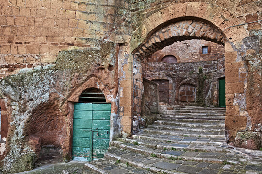 Pitigliano, Tuscany, Italy: Medieval city gate Porta di Sovana with stone stairs and cellar doors, in the village founded in Etruscan times