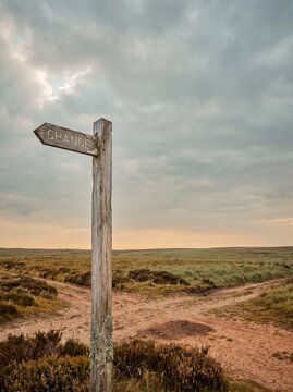 Wooden signpost Change arrow at fork in dirt path on moorland