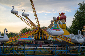 Swan-shaped ride with yellow support structure. Colorful amusement park ride with swan figures. Set against twilight sky and green trees. Ride includes multiple swans in different positions © vefimov