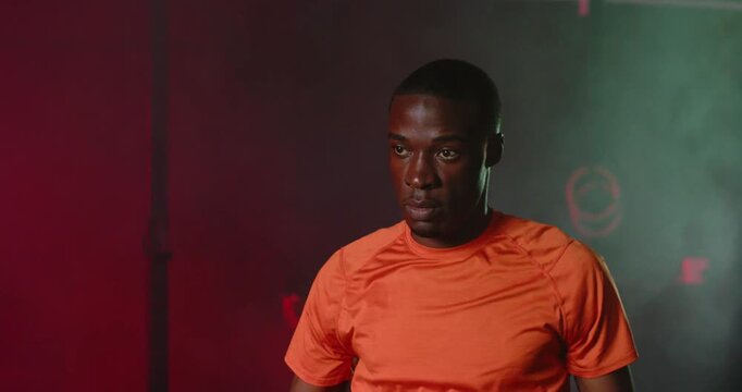Man warming in studio in orange-shirt pulling right arm holding triceps stretch preparing workout