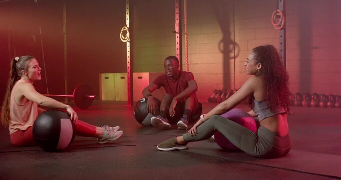 Diverse gymmates in sportswear sitting with medicine balls and stability ball, resting between sets