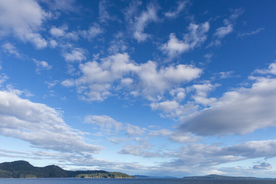 Blue Sky With Scattered Clouds Over Gulf Islands Sea and Forested Shoreline in British Columbia, Canada
