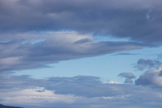 Dramatic Blue Cloudscape Over Layered Clouds With Soft Light And Distant Forest Horizon