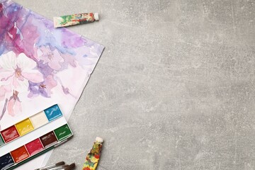 Naklejka premium Different brushes, watercolor paints, tubes and drawing on grey table, flat lay. Space for text