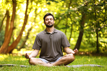 Obraz premium Handsome man practicing yoga on mat in park