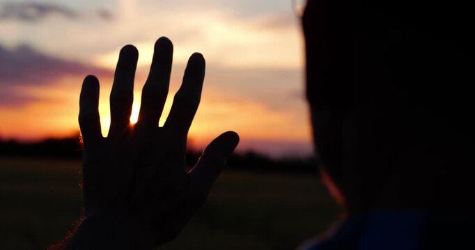 Man reaches toward glowing sunset above open field, embracing dreams and future possibilities. Warm evening landscape symbolizes aspiration, imagination, hope and pursuit of meaningful goals.