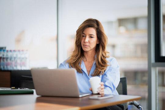 Confident middle-aged businesswoman using her laptop in a modern office