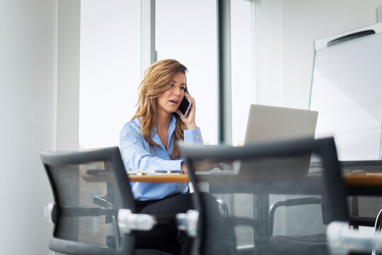 Blond haired mature businesswoman working on her laptop and using a smartphone at office desk