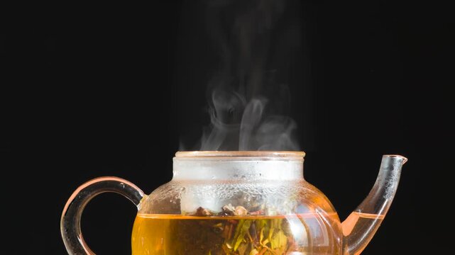 Teapot With Fresh Tea. Steam slowly rises from a glass teapot with freshly brewed tea on a black background