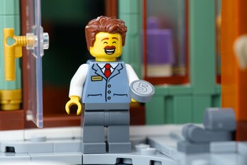 Fototapeta premium Tambov, Russian Federation - June 28, 2026 A cheerful Lego man minifigure with a mustache standing outside a building holding a five value coin