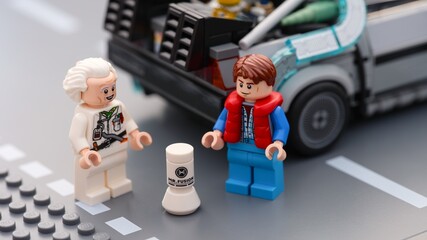Fototapeta premium Tambov, Russian Federation - July 12, 2026 Lego minifigures of Doc Brown and Marty McFly standing on a road next to the Mr. Fusion home energy reactor and the DeLorean time machine car.