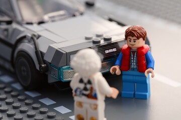 Fototapeta premium Tambov, Russian Federation - July 12, 2026 A Lego Marty McFly minifigure standing next to the DeLorean time machine car while looking at Doc Brown from behind.
