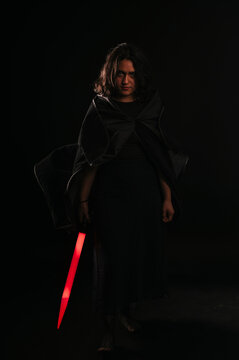 Vertical portrait of a girl cosplaying as a Sith from the Star Wars saga, with her lightsaber beside her pointing downwards.
