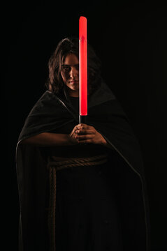 Vertical portrait of a girl cosplaying as a Sith from the Star Wars saga, with her lightsaber held in front of her. Her eyes have already turned orange-red due to her conversion.

