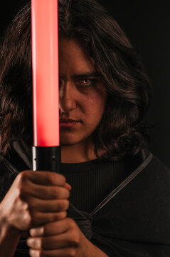 Vertical portrait of a girl cosplaying as a Sith from the Star Wars saga, with her lightsaber held in front of her. Her eyes have already turned orange-red due to her conversion.
