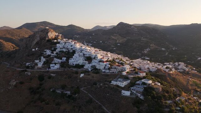 Golden hour sunlight illuminating the traditional white cycladic houses of ios chora village, a picturesque town nestled on a hillside in the greek islands during a beautiful summer sunset