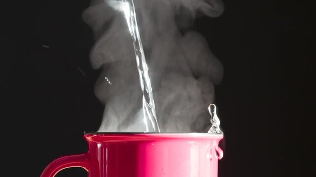 Coffee in a Red Mug. A jet of boiling water falls into a red ceramic mug, creating puffs of white steam against a black background