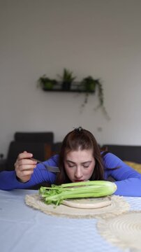Vertical screen Young woman with eating disorder stares at plain celery because calorie obsession leaves her believing this is the only food she is allowed to eat