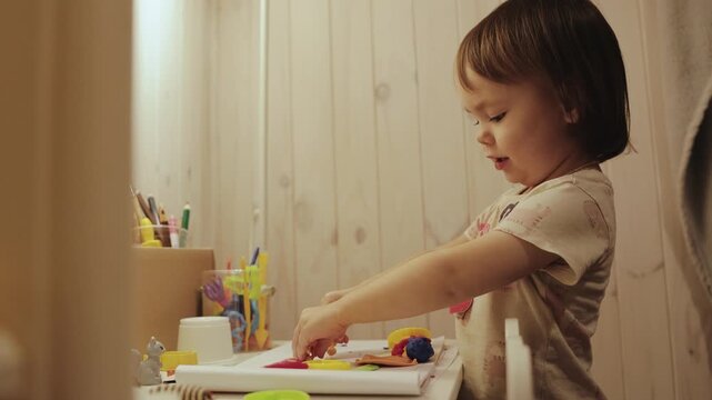 Little girl enjoying quiet playtime at a small desk in her room with toys and creative activities.