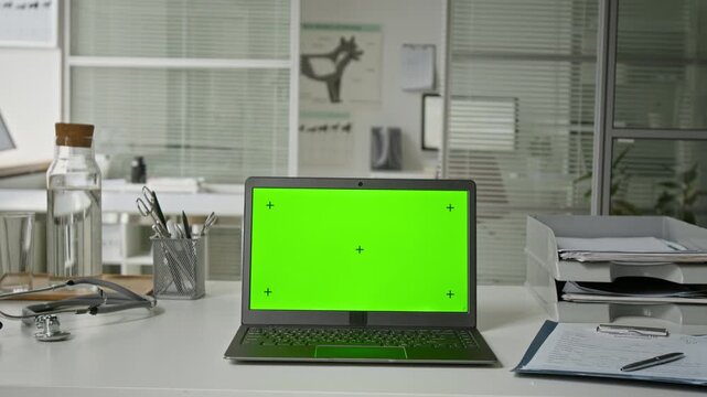 Laptop with green screen sitting on desk in veterinary clinic with stethoscope nearby. Mockup screen allowing integration of pet care software or online veterinary consultation services