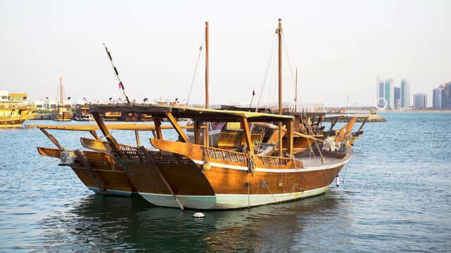 A scenic wide shot of traditional wooden dhow boats moored in the calm, blue waters of Doha Bay. The image beautifully captures the contrast between Qatar&rsquo;s rich maritime heritage and the sleek.