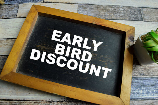 Chalkboard with phrase early bird discount and school supplies on wooden desk