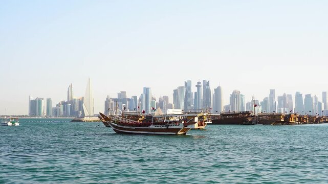 A scenic view across Doha Bay capturing traditional wooden dhow boats resting on calm blue waters in the foreground, contrasted against the impressive, modern skyscrapers of the Doha city skyline.