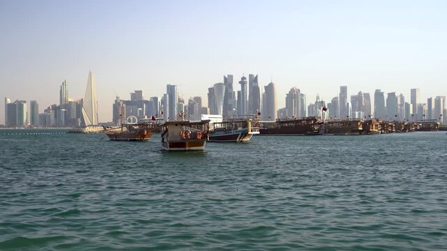 A scenic panoramic view of Doha Bay, featuring a collection of traditional wooden dhow boats moored in the foreground contrasted against the modern, towering skyscraper skyline of Doha, Qatar.