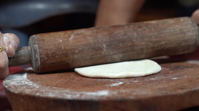 Close Up of Rolling Small Flour Dough Ball with Wooden Pin on Chakla Board. Indian Housewife Hands Rolling Small Dough Portion with Wooden Belan on Board. Step by Step Process of Rolling Out Raw Wheat