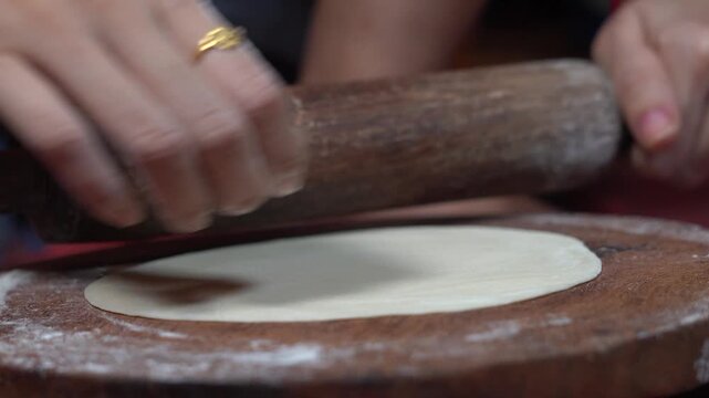 Close Up of Indian Woman Hands Rolling Dough with Wooden Pin on Chakla Board. Traditional Method of Rolling Out Wheat Flour Dough for Roti or Chapati.
