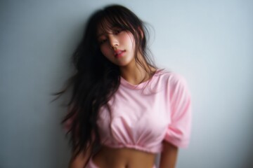 Fototapeta premium Young attractive asian woman with long dark hair wearing pink crop top posing against light studio background with soft even lighting looking at camera