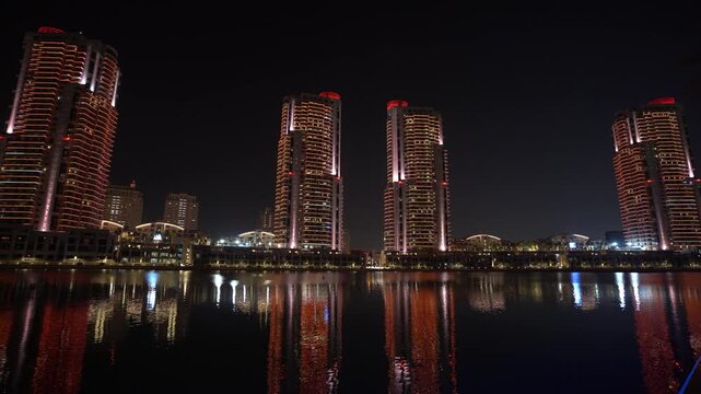 A scenic night-time panoramic view of The Pearl-Qatar waterfront, featuring a row of elegantly illuminated high-rise residential towers glowing warmly against the dark evening sky.