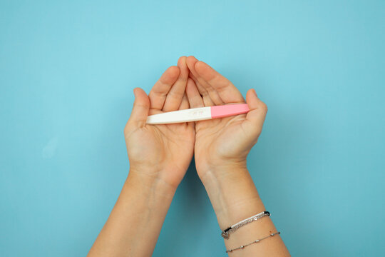 hands cupped together holding a positive pregnancy test against a blue background with copy space concept of maternity family planning wellness anticipation medical advertisement banner