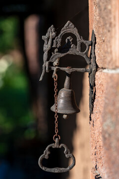 Vintage cast iron doorbell with chain on stone wall, closeup. Antique bronze door bell hanging on rustic brick wall with a decorative metal bracket and pull chain