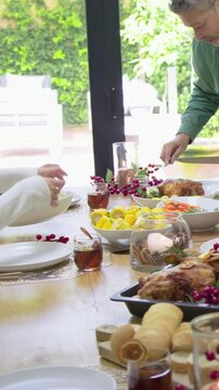 Vertical video: Reaching guests as host in green shirt carving roast at home table with fork, knife
