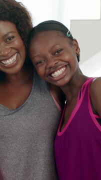 Vertical video: Smiling mother and daughter leaning closer at home, camera rolling, posing in tanks